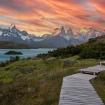Wooden boardwalk leading to Torres del Paine mountains under a vibrant sunset sky in Chile.