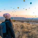 Woman watching hot air balloons in Cappadocia at sunrise, a popular travel destination.
