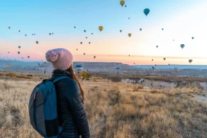 Woman watching hot air balloons in Cappadocia at sunrise, a popular travel destination.