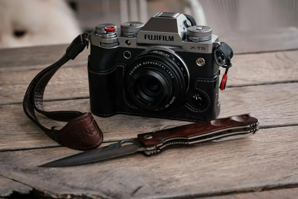 Fujifilm X-T5 camera with lens and folding knife on a rustic wooden table.