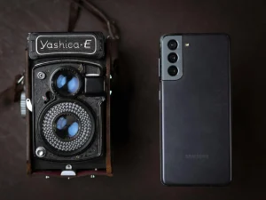 A vintage Yashica camera next to a modern smartphone, showcasing old and new technology.