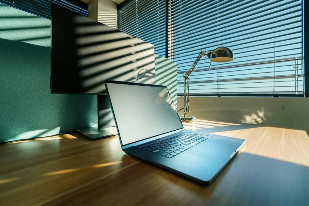 A clean, sunlit office desk with a modern laptop and monitor, perfect for business or corporate settings.