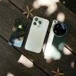 Three modern smartphones displayed on a wooden surface with natural lighting.