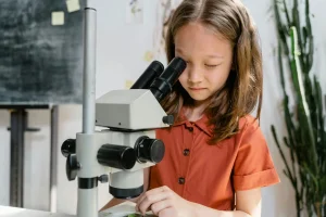 A curious girl examining a sample using a microscope in a classroom setting, focused on learning science.