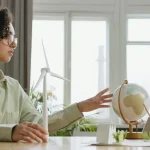 A young woman explores renewable energy with a globe and wind turbine model indoors.