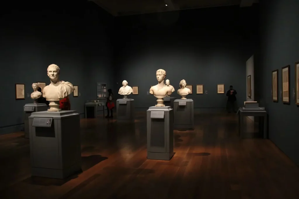 An art gallery with classical sculptures and framed art, showcasing elegant indoor lighting and design.