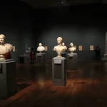 An art gallery with classical sculptures and framed art, showcasing elegant indoor lighting and design.